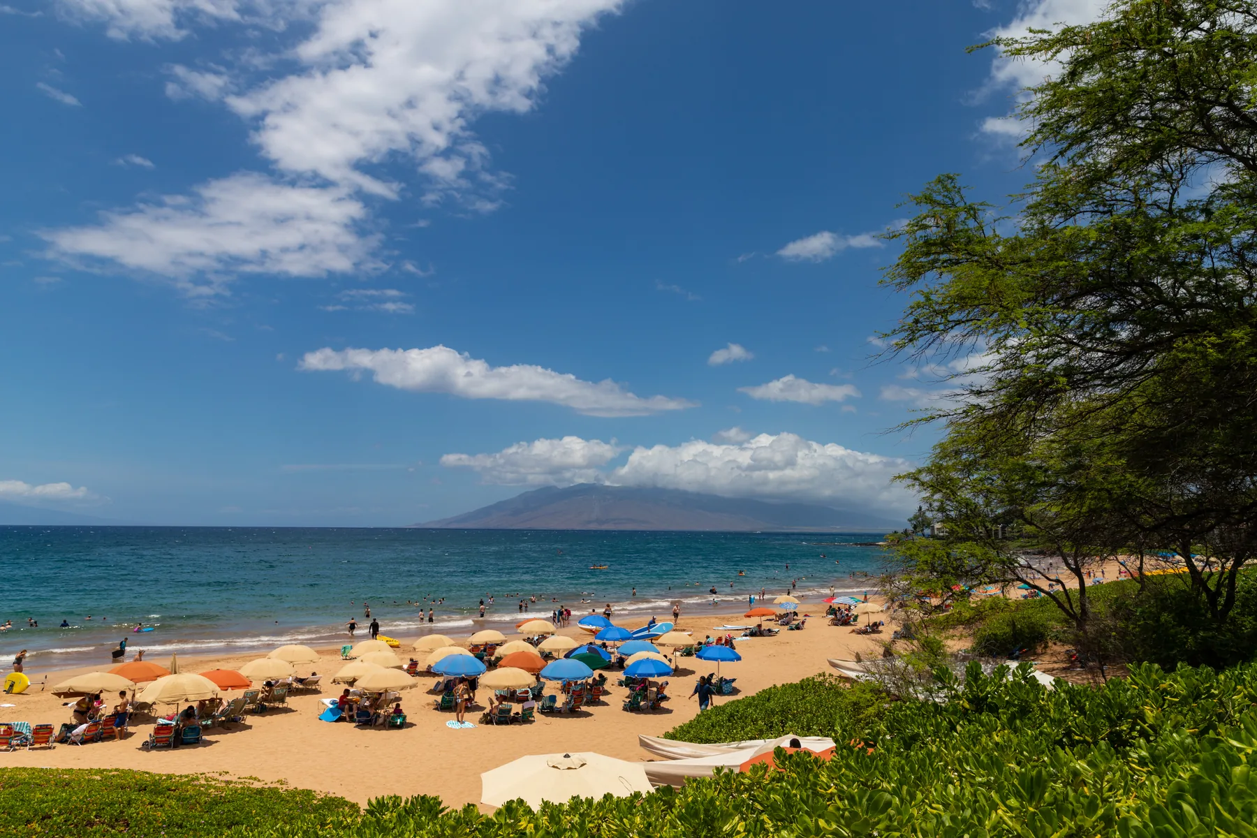 Wailea beach on a sunny day with resort umbrellas and the West Maui mountains beyond