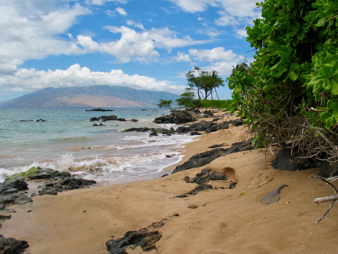 Kihei shoreline with black lava rock, golden sand and the West Maui mountains across the channel